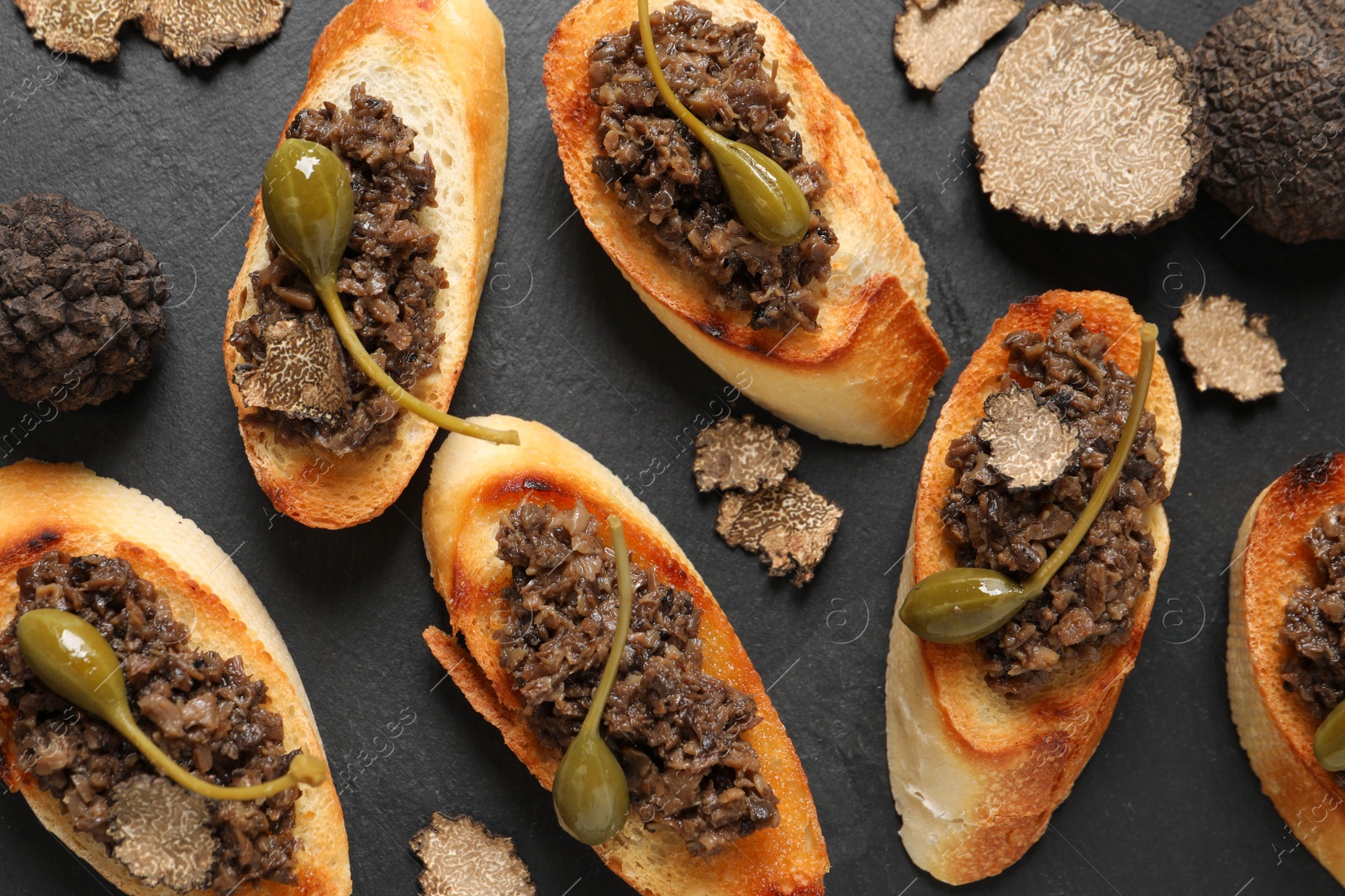 Photo of Tasty bruschettas with truffle paste and capers on black table, flat lay