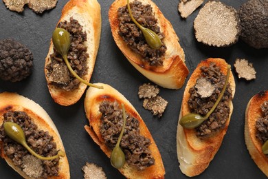 Photo of Tasty bruschettas with truffle paste and capers on black table, flat lay