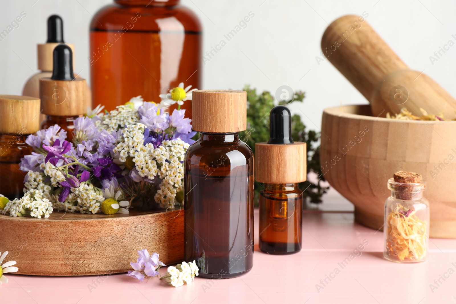 Photo of Aromatherapy. Different essential oils, mortar, pestle and flowers on pink wooden table