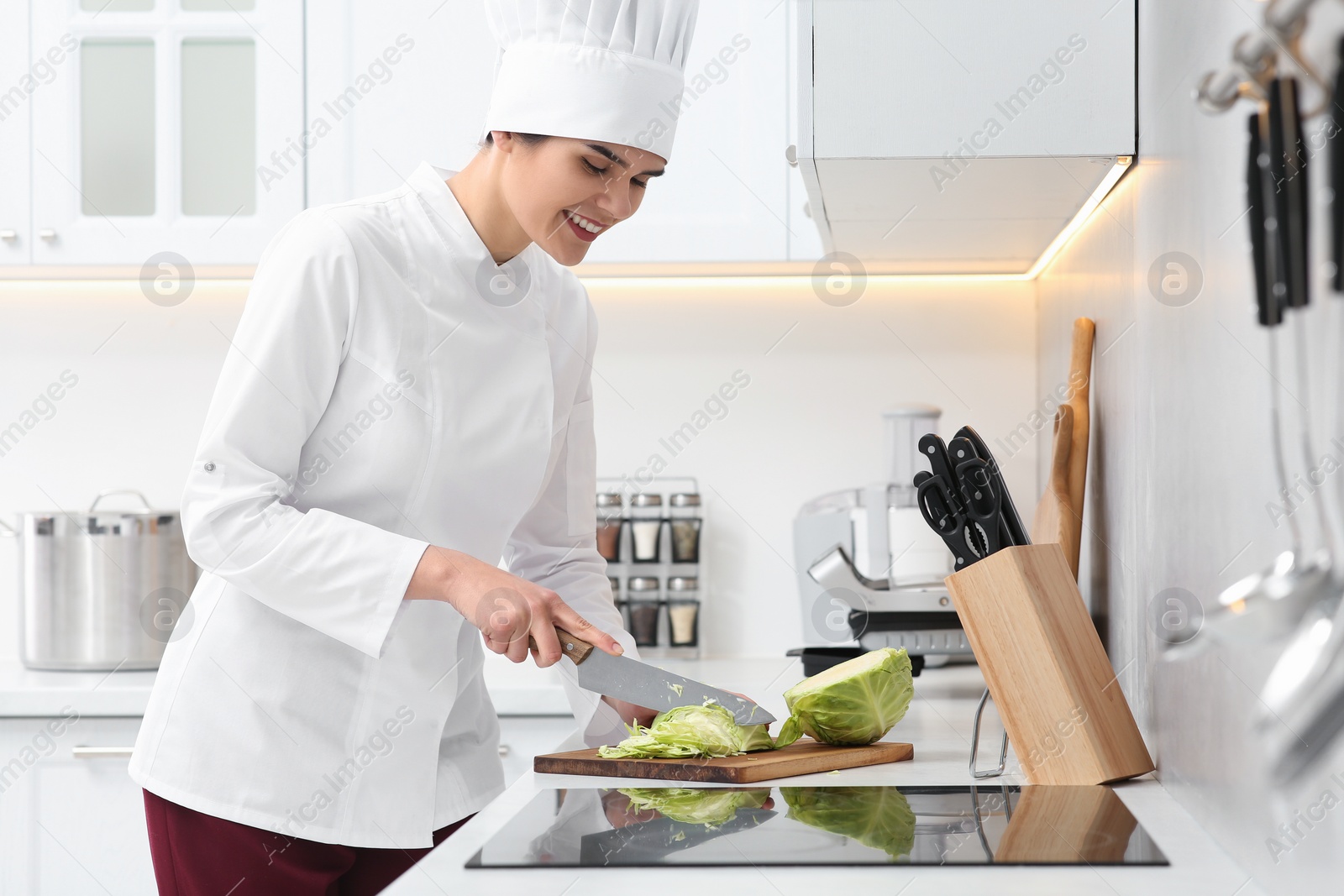 Photo of Professional chef cutting cabbage at white countertop in kitchen