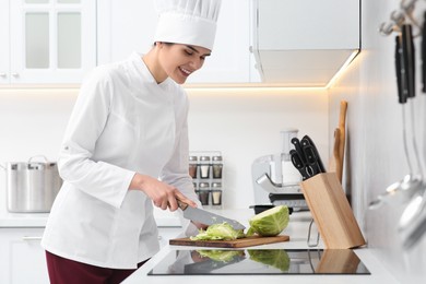Photo of Professional chef cutting cabbage at white countertop in kitchen