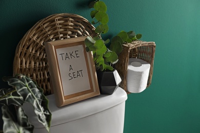 Decor elements, paper rolls and toilet bowl near green wall, space for text. Bathroom interior