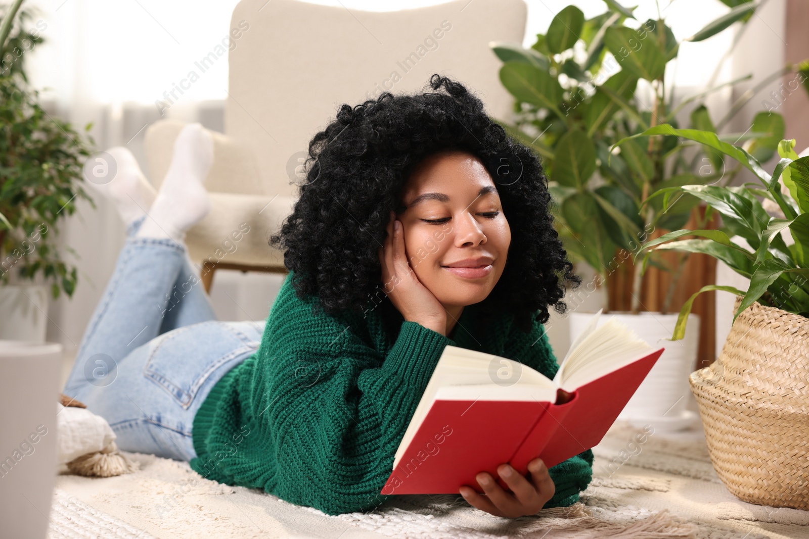 Photo of Relaxing atmosphere. Woman reading book near potted houseplants at home