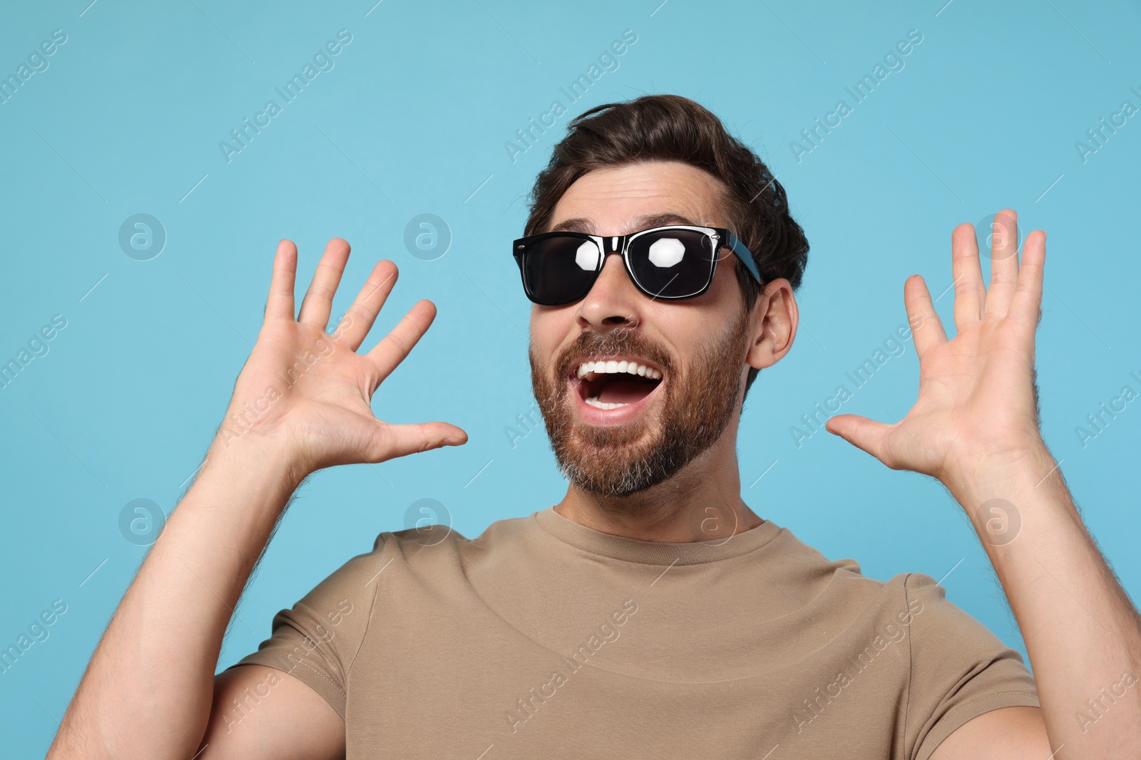 Photo of Portrait of excited bearded man with stylish sunglasses on light blue background