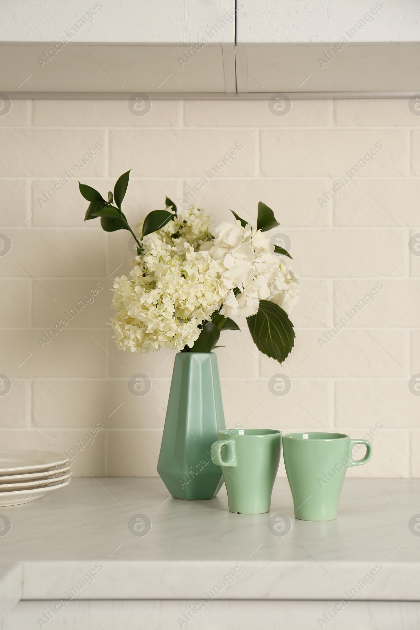 Photo of Bouquet with beautiful white hydrangea flowers and cups on light countertop