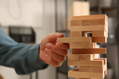 Playing Jenga. Woman removing wooden block from tower indoors, closeup