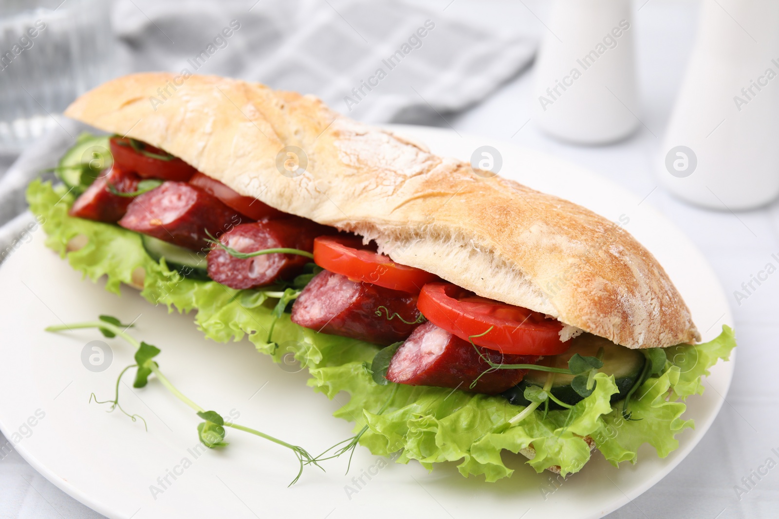 Photo of Delicious sandwich with sausages and vegetables on white table, closeup