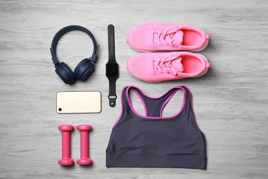Photo of Stylish sportswear, dumbbells and smartphone on wooden background, flat lay