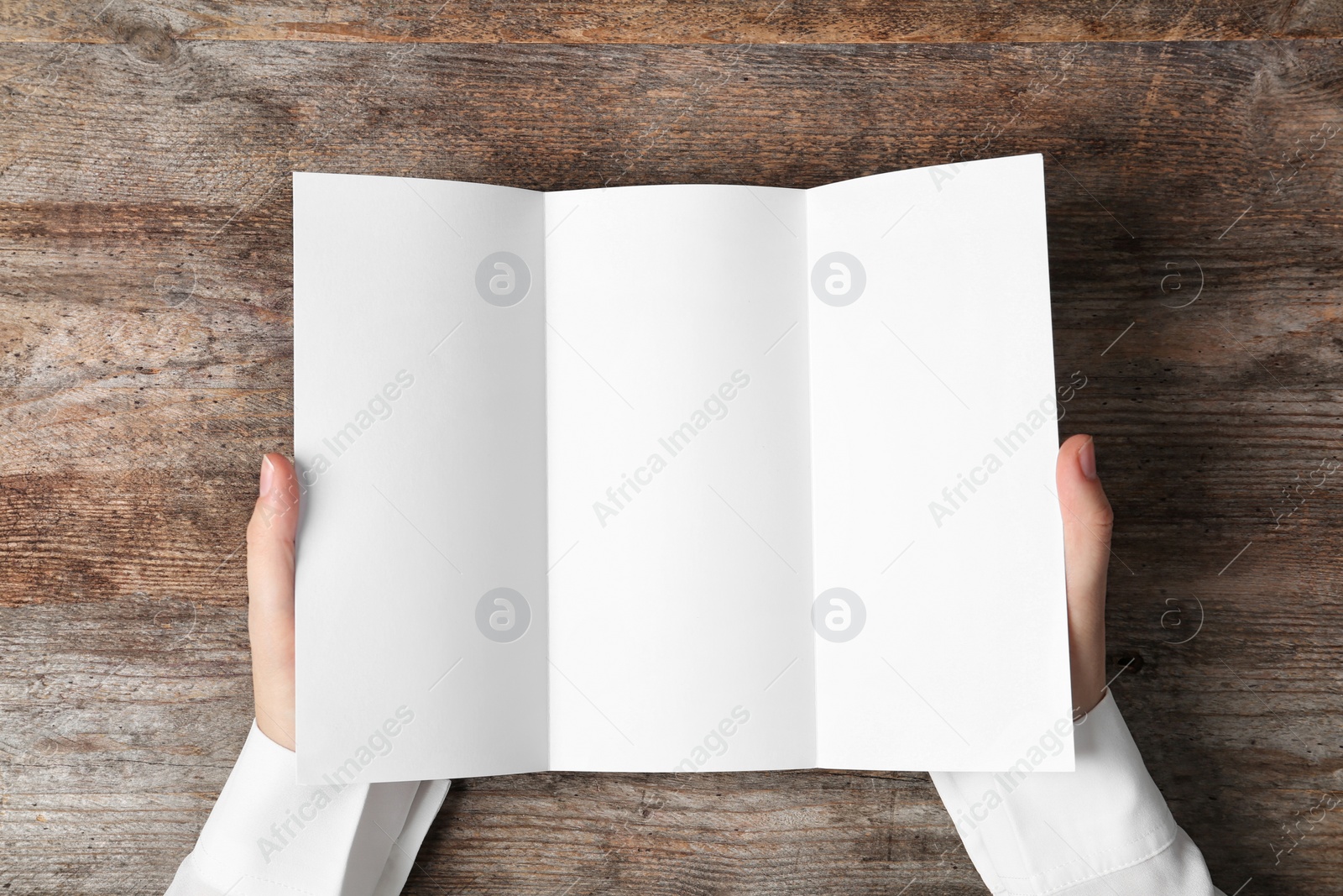 Photo of Woman holding blank brochure mock up on wooden table, top view