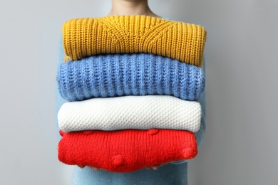 Woman holding pile of winter sweaters on grey background, closeup view