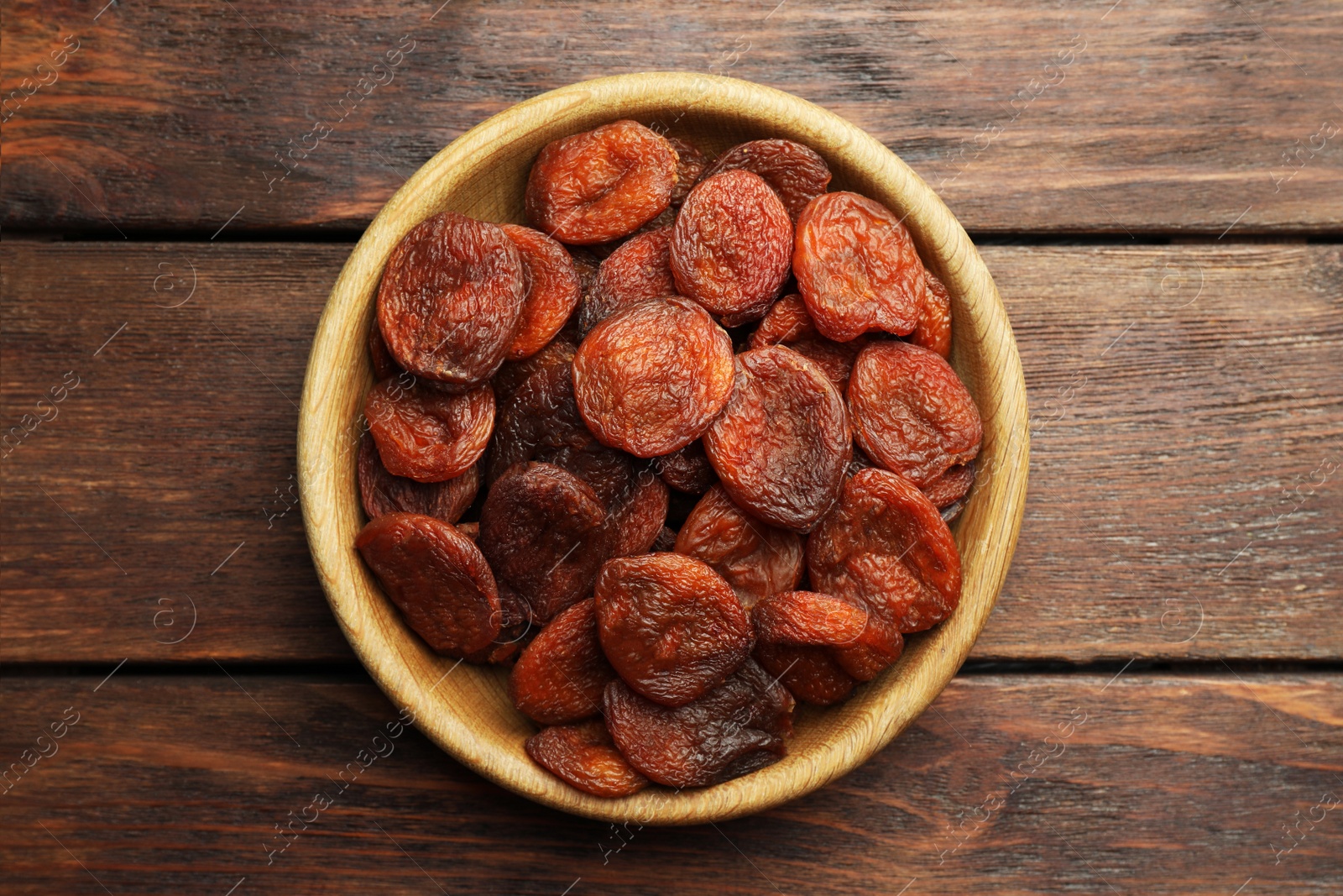 Photo of Bowl of tasty apricots on wooden table, top view. Dried fruits