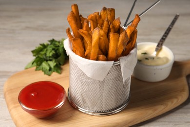 Photo of Frying basket with sweet potato fries, sauces and parsley on table, closeup