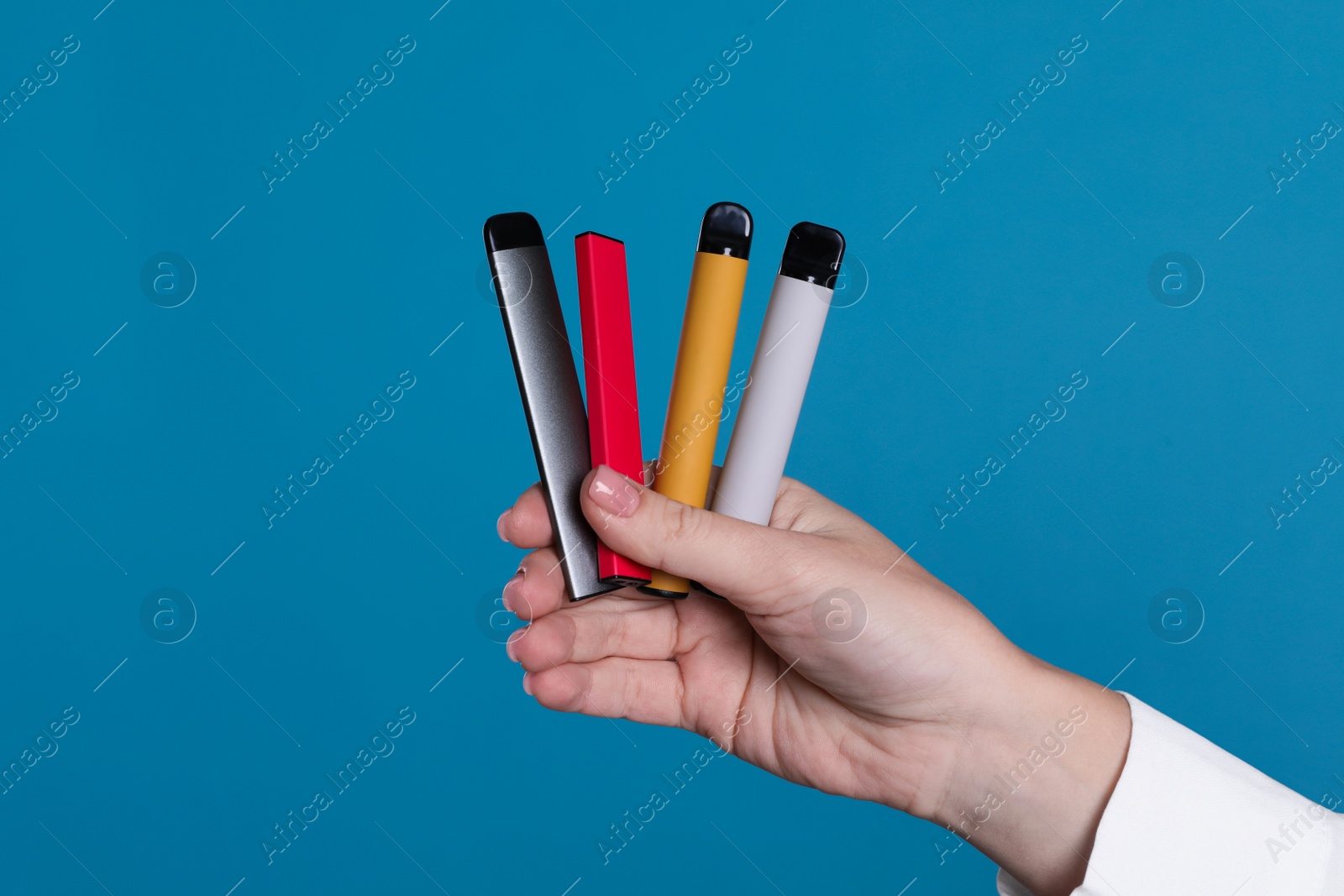 Photo of Woman holding different electronic cigarettes on light blue background, closeup