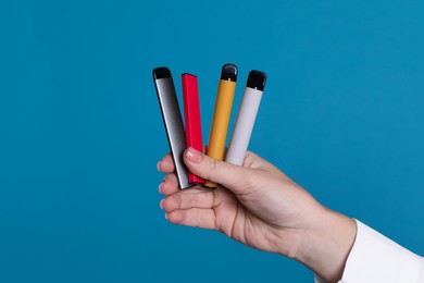 Woman holding different electronic cigarettes on light blue background, closeup