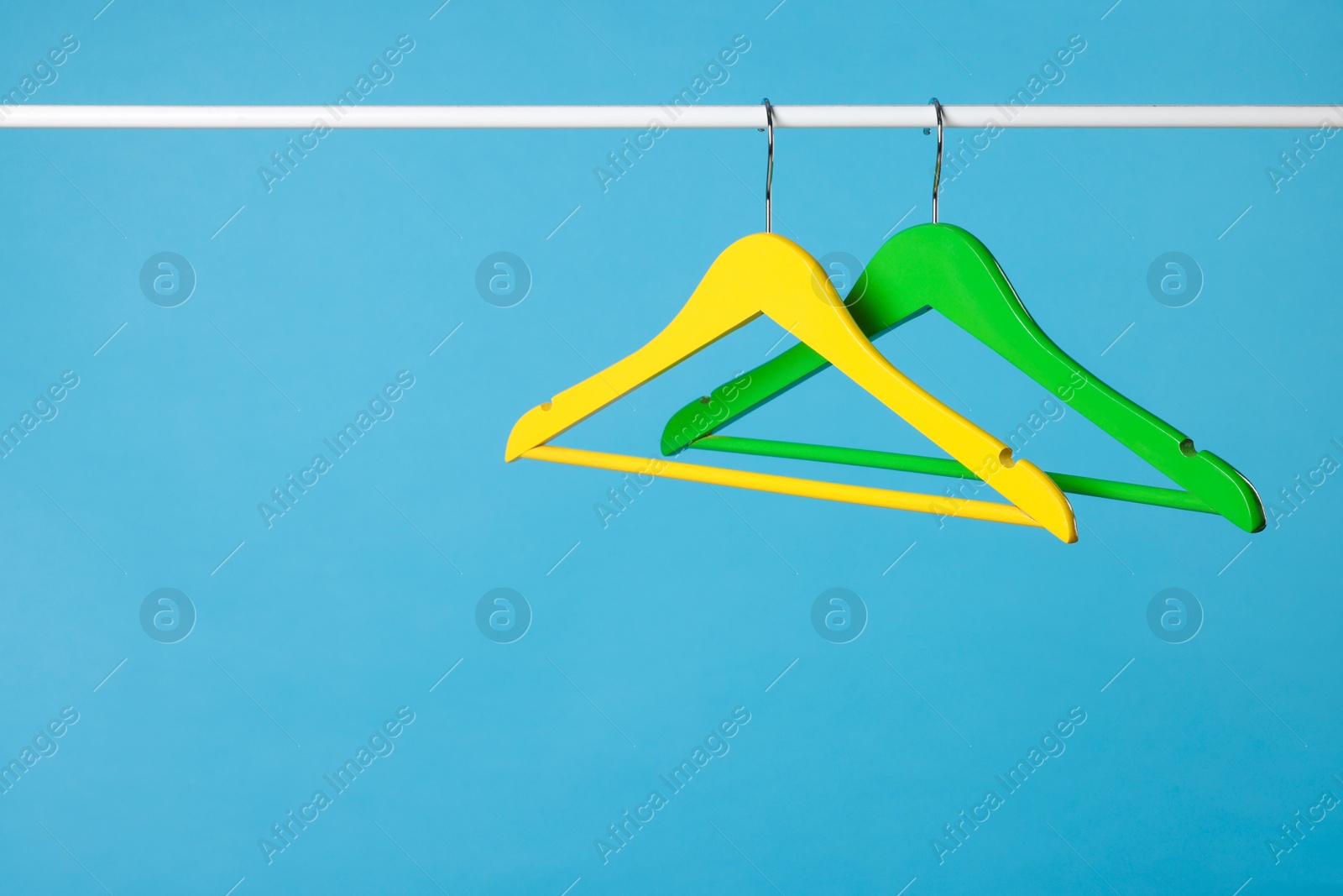 Photo of Bright clothes hangers on metal rail against light blue background. Space for text