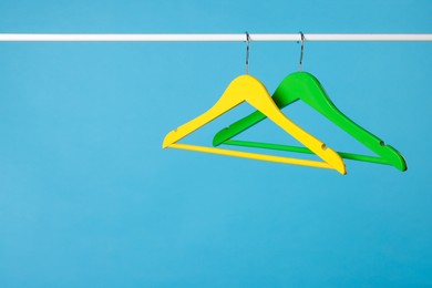 Photo of Bright clothes hangers on metal rail against light blue background. Space for text