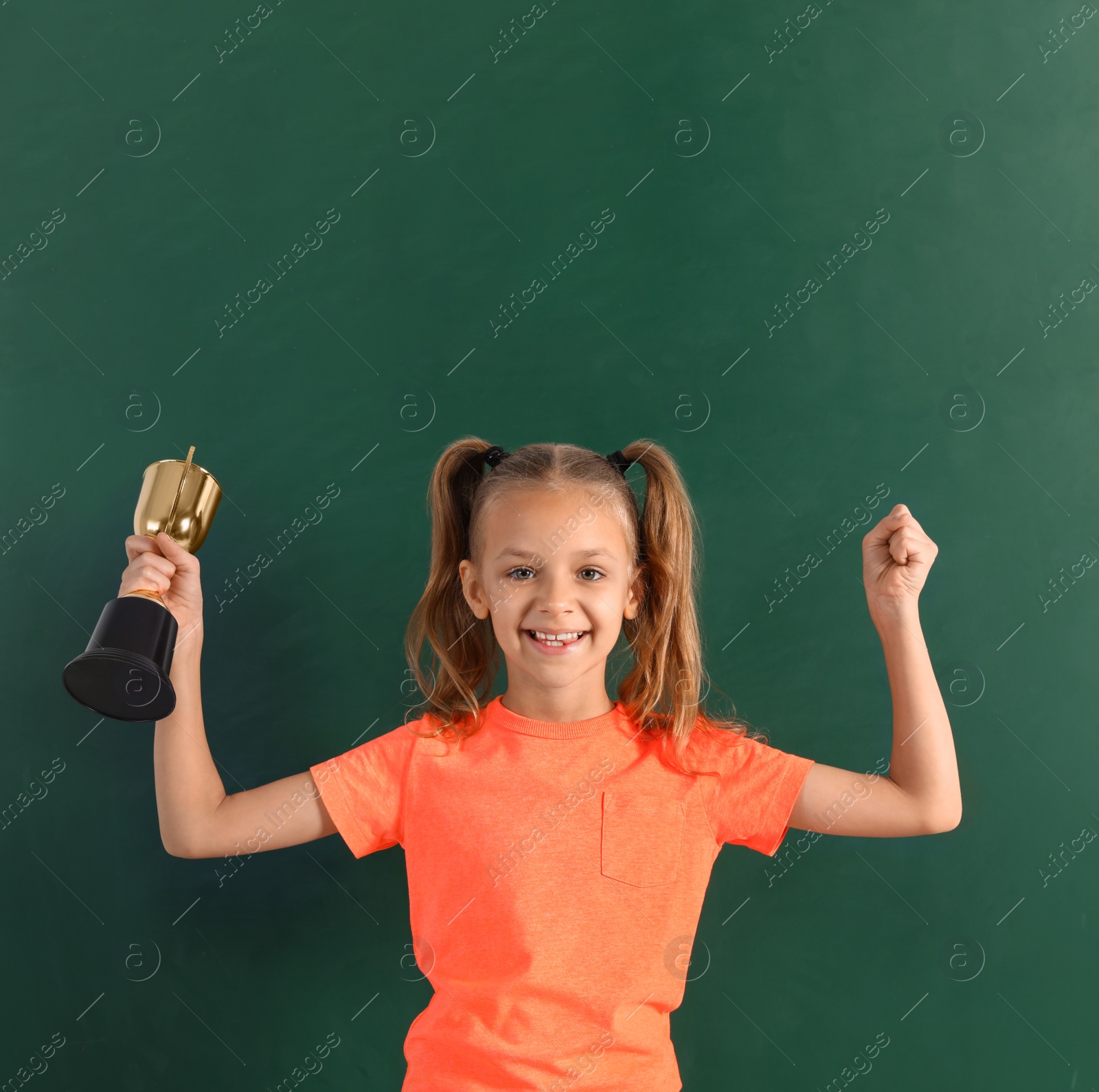 Photo of Happy girl with golden winning cup near chalkboard