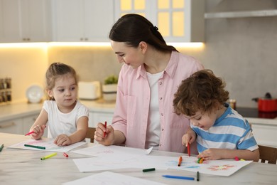 Photo of Mother and her little children drawing with colorful markers at table in kitchen