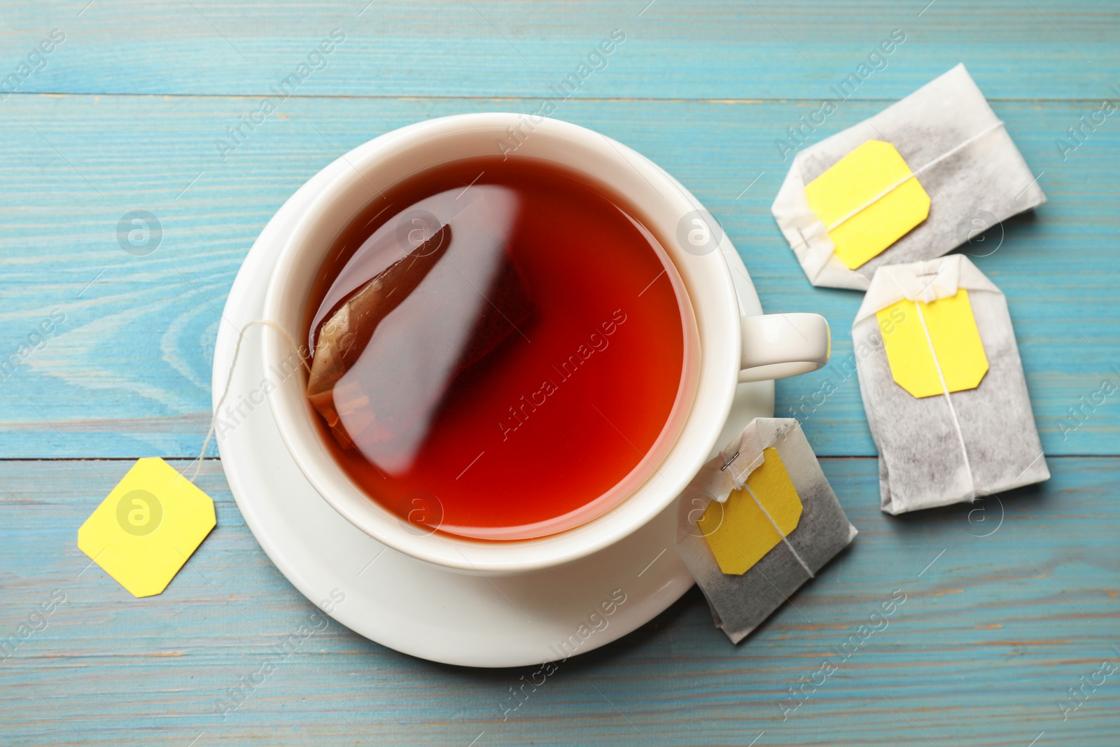 Photo of Tea bags and cup with hot drink on light blue wooden table, top view