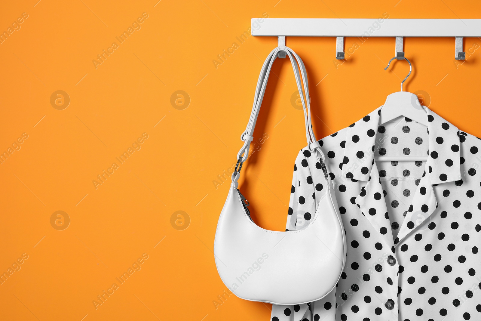 Photo of Hanger with polka dot shirt and bag on orange wall, space for text