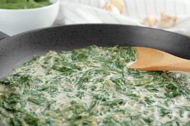 Photo of Tasty spinach dip with wooden spoon in frying pan, closeup view