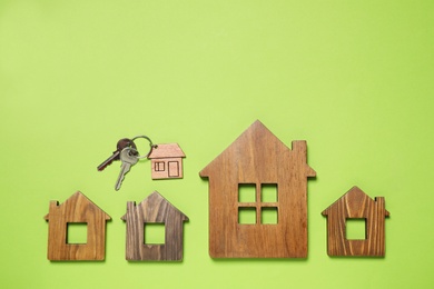 Photo of House models and keys on light green background, flat lay. Space for text