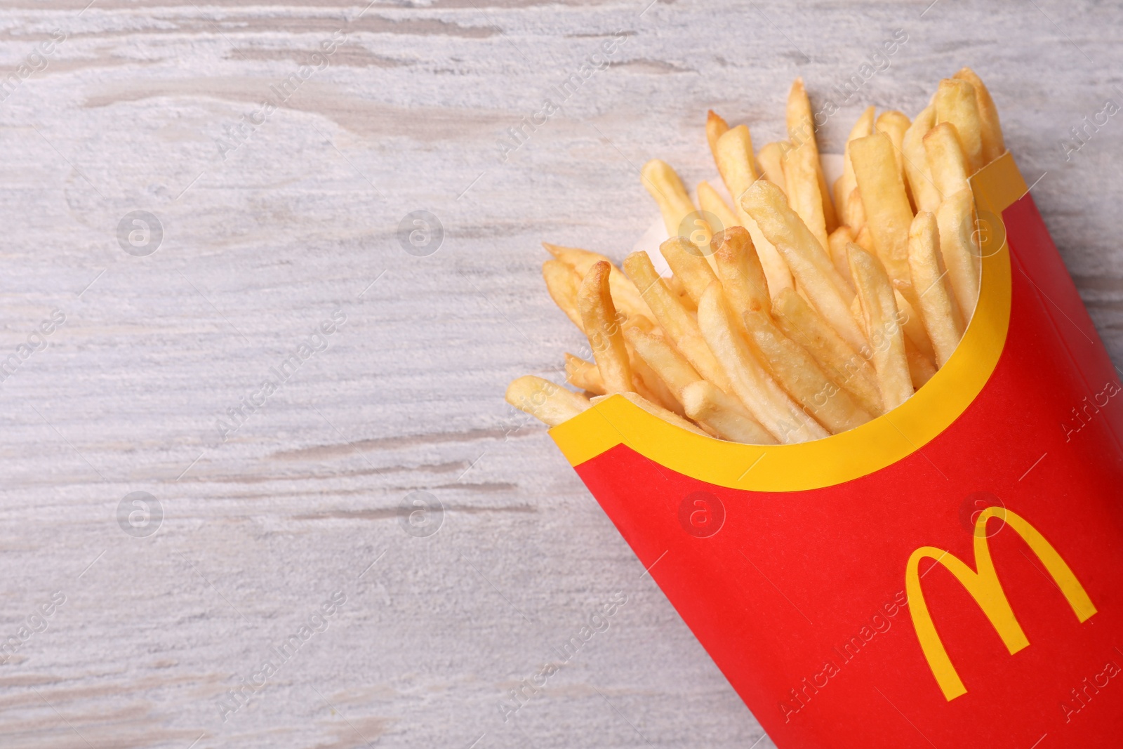 Photo of MYKOLAIV, UKRAINE - AUGUST 12, 2021: Big portion of McDonald's French fries on white wooden table, top view. Space for text