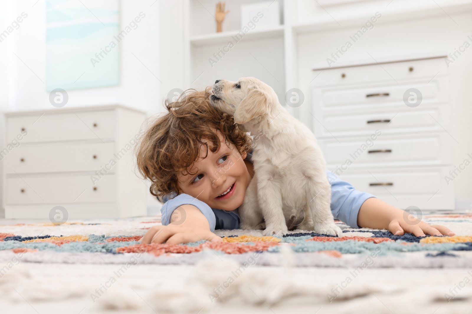 Photo of Little boy lying with cute puppy on carpet at home