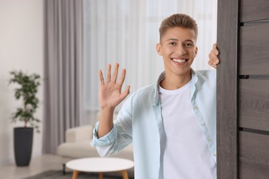 Photo of Happy man waving near door, space for text. Invitation to come indoors