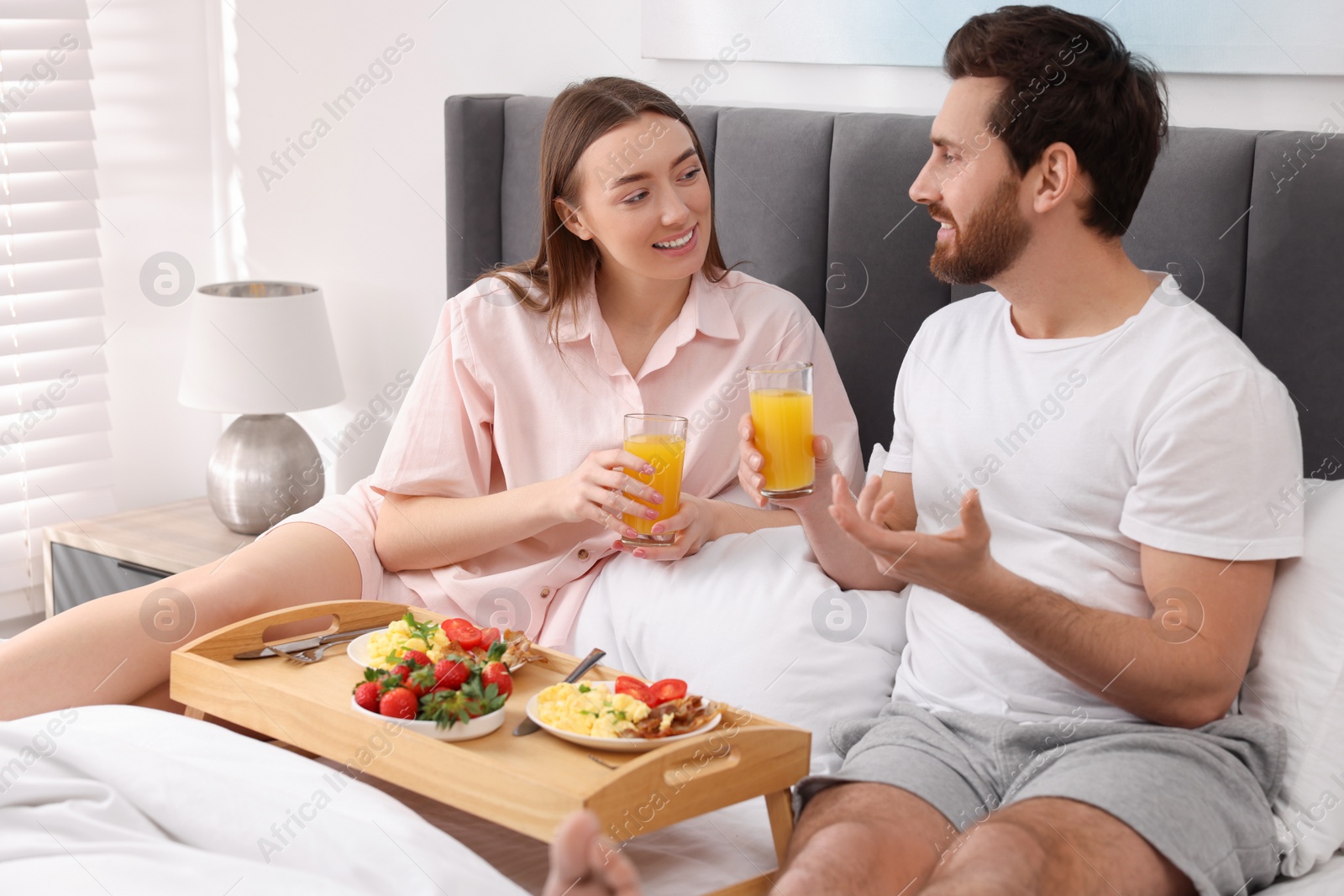 Photo of Happy couple having breakfast and talking on bed at home