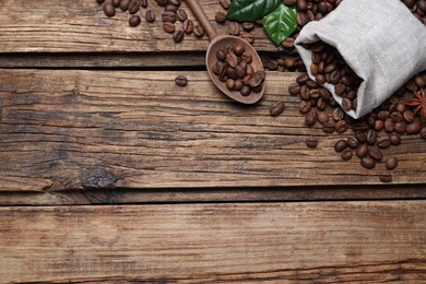 Photo of Bag of roasted coffee beans, spoon and green leaves on wooden table, flat lay. Space for text