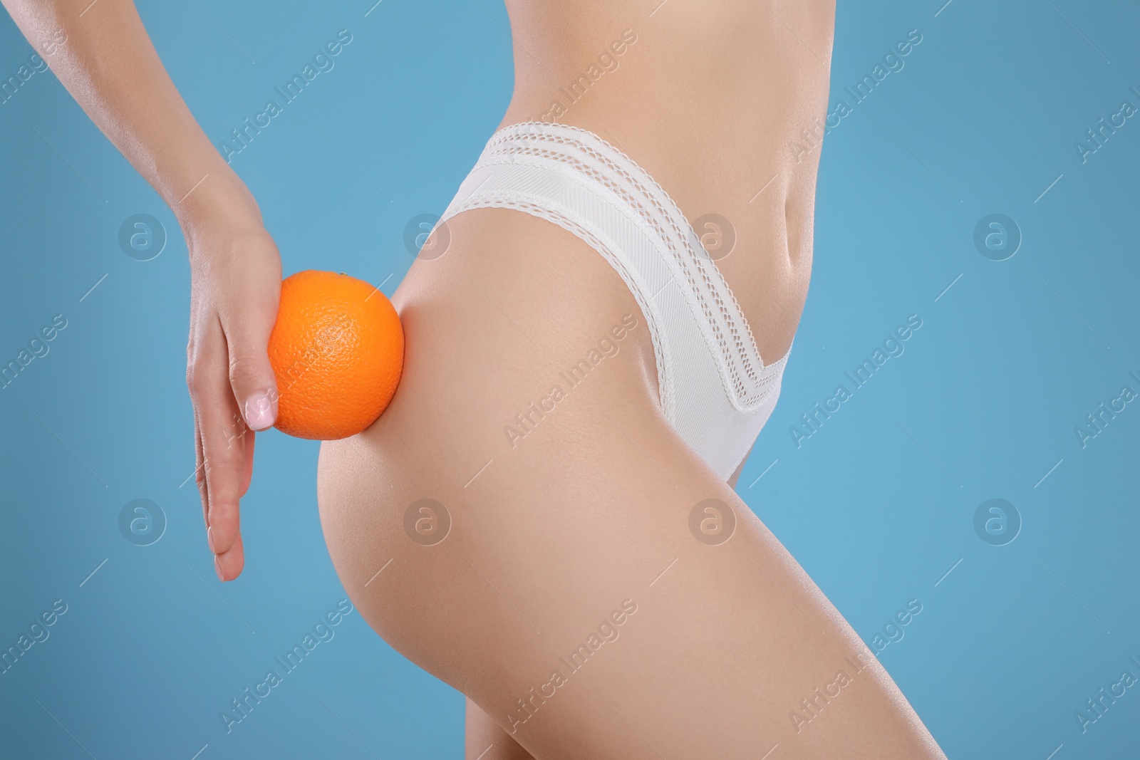 Photo of Closeup view of slim woman in underwear with orange on light blue background. Cellulite problem concept