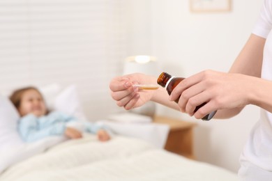 Photo of Mother pouring cough syrup into measuring spoon for her daughter in bedroom, focus on hands