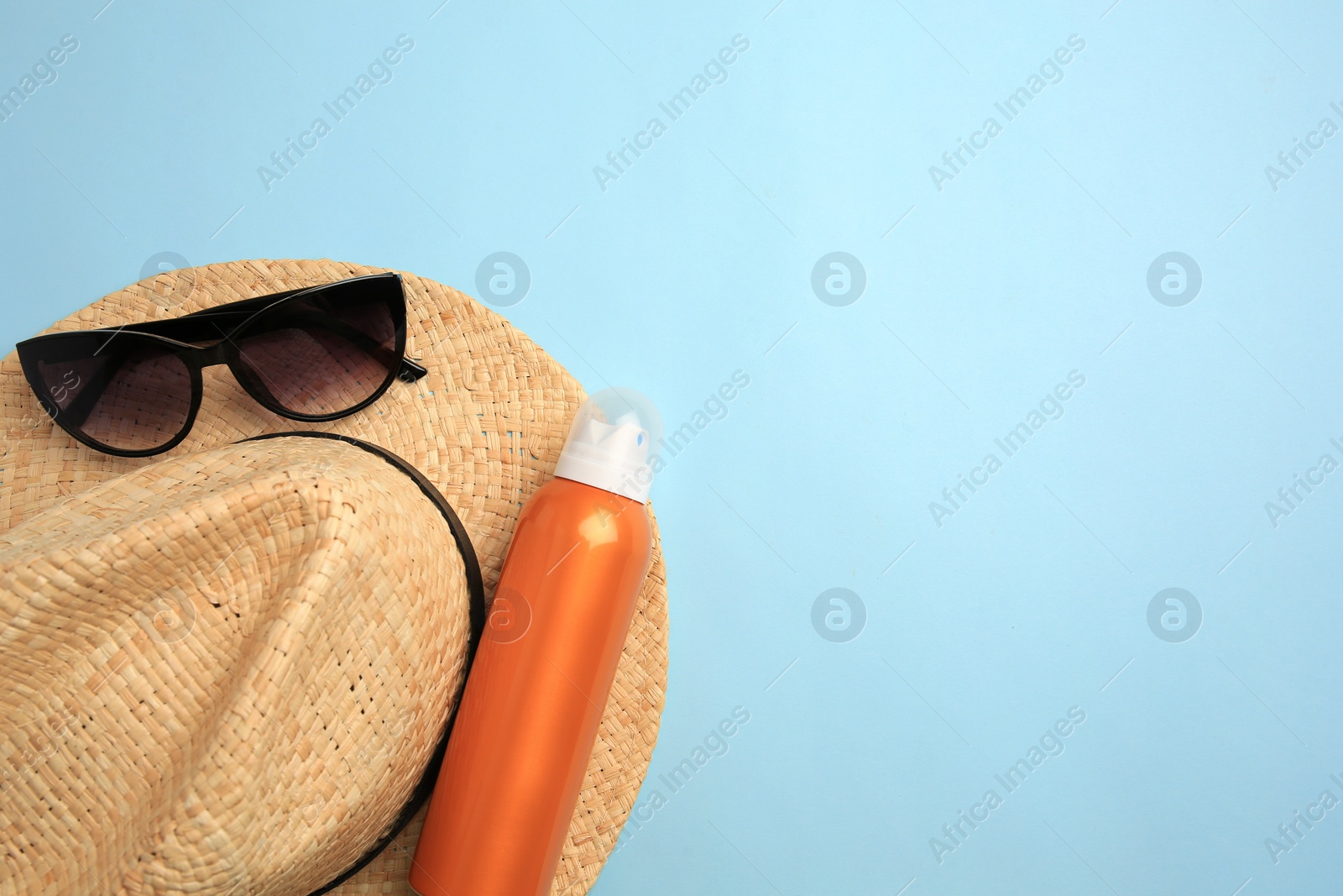 Photo of Bottle of sunscreen and beach accessories on light blue background, top view. Space for text