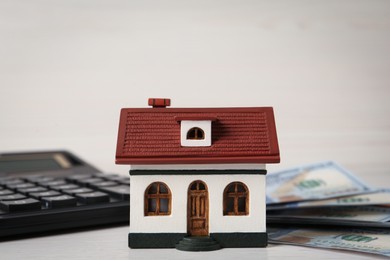 Photo of Mortgage concept. House model, calculator and money on white wooden table, closeup