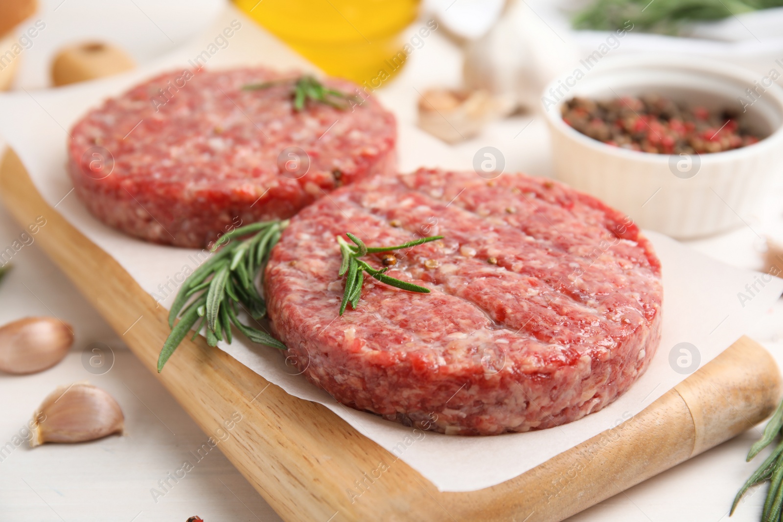 Photo of Raw hamburger patties with rosemary on white wooden table, closeup