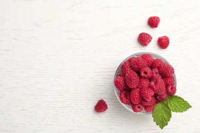 Photo of Bowl with ripe aromatic raspberries on wooden table, top view