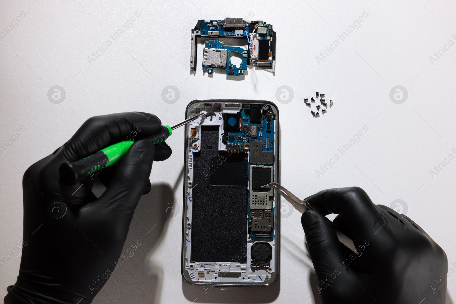 Photo of Technician repairing broken smartphone at white table, top view