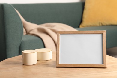 Photo of Empty square frame and candles on wooden table indoors, space for text