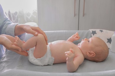 Mother changing baby's diaper on table indoors, closeup