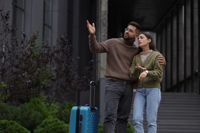 Being late. Worried couple with suitcase near building outdoors, space for text