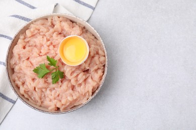 Photo of Fresh raw minced meat, parsley and egg in bowl on light grey table, top view. Space for text