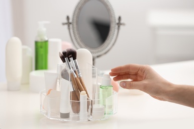 Woman reaching for organizer with cosmetic products and makeup accessories on dressing table indoors, closeup