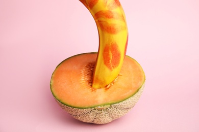 Photo of Fresh banana with red lipstick marks and melon on pink background. Sex concept