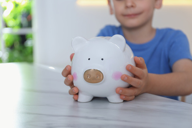 Photo of Little boy with piggy bank at marble table indoors, closeup