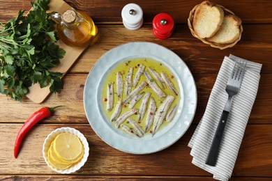 Photo of Tasty pickled anchovies with spices and products on wooden table, flat lay