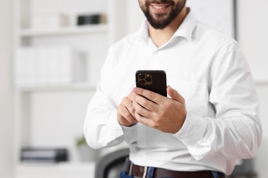 Young man using smartphone in office, closeup. Space for text