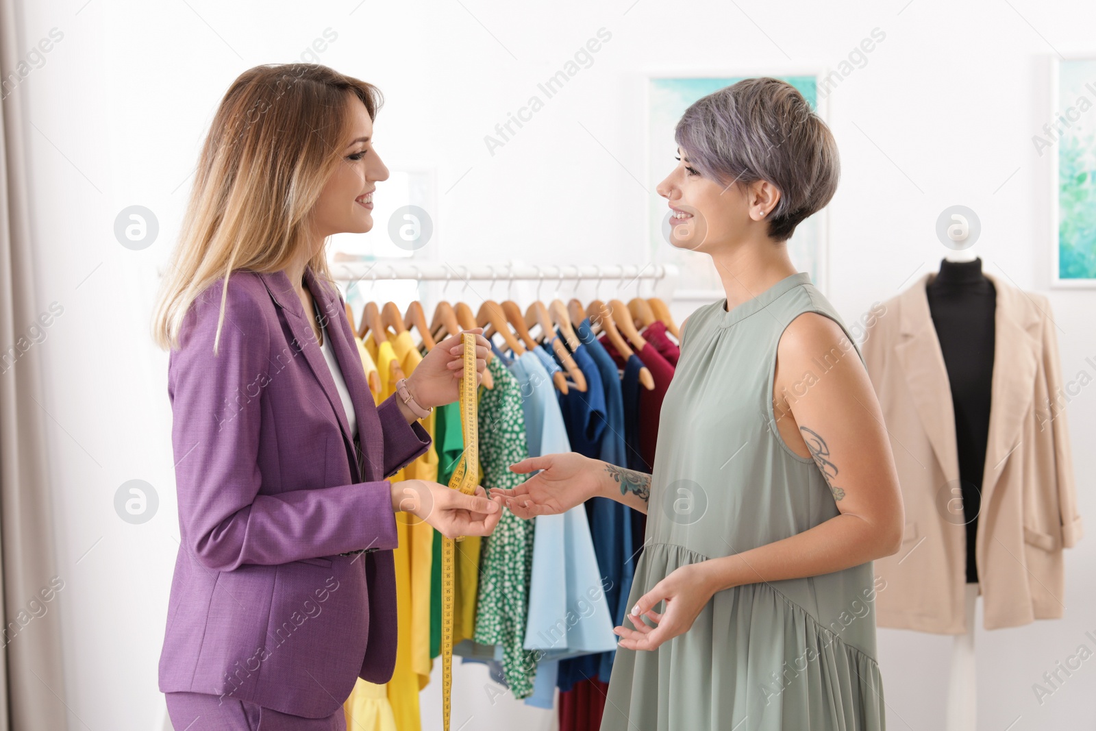 Photo of Beautiful young stylist and client near rack with clothes in studio