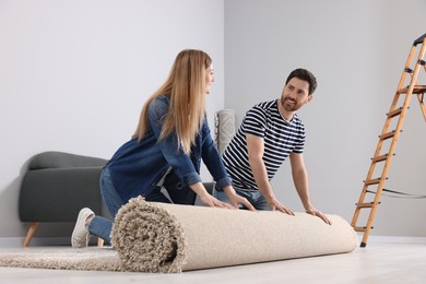 Photo of Smiling couple unrolling new carpet in room