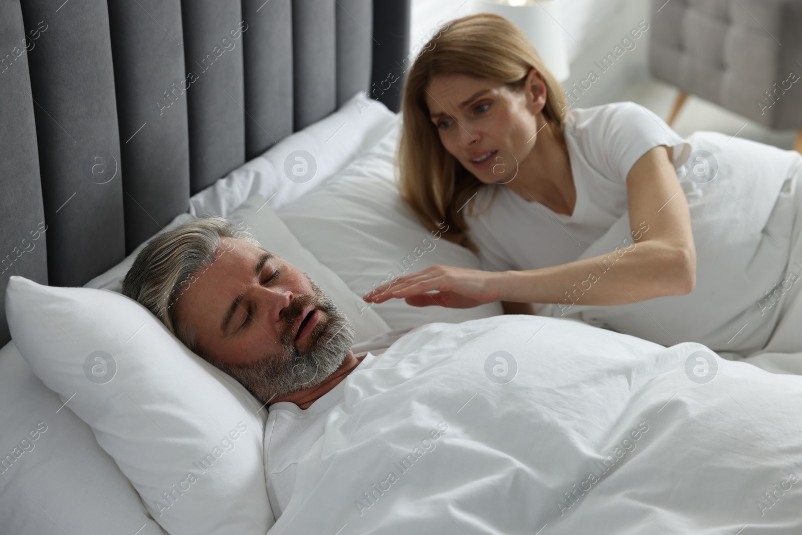 Photo of Irritated woman waking up her snoring husband in bed at home